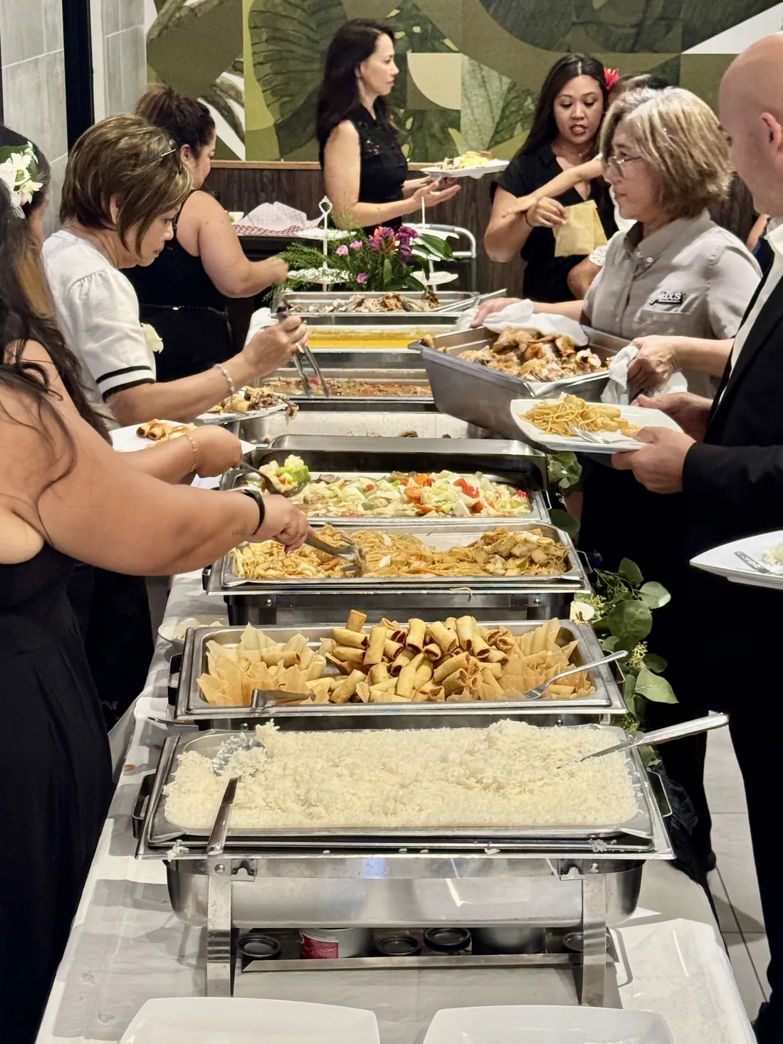 Guests serving themselves rice, lumpia, pancit and vegetables from chafing trays at Max's San Diego